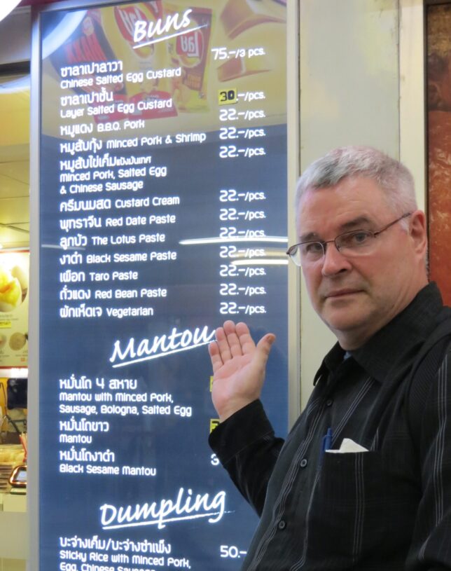Our B2B Food Writing copywriter, Bill is showing the food menu at the food court in Bangkok, Thailand