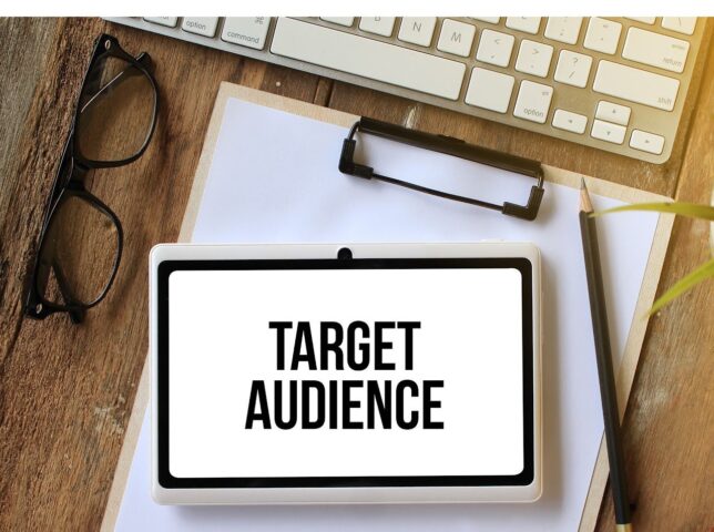 A small sign "target audience" sitting on a clipboard, besides a keyboad, reading glasses and a pencil