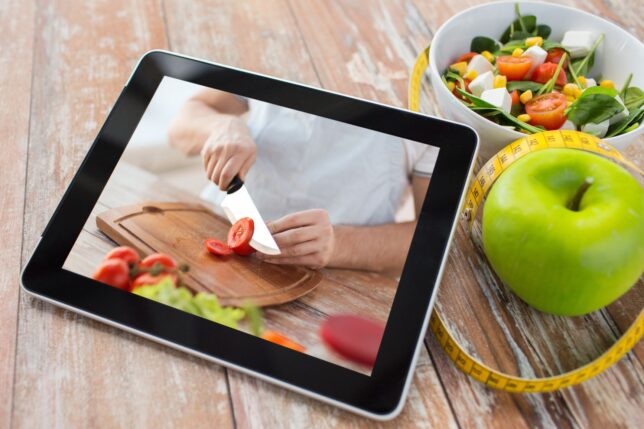 Image about engaging video sales letters showing a tablet with a picture of a person cutting tomatoes propped up next to a green apple and salad