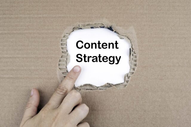 A finger pointing at "Content Strategy" on a white paper placed in the middle of a torn-out cardboard
